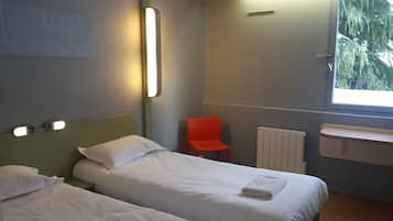 A hotel room with two single beds, a red chair, a radiator, and a window with a view of trees.