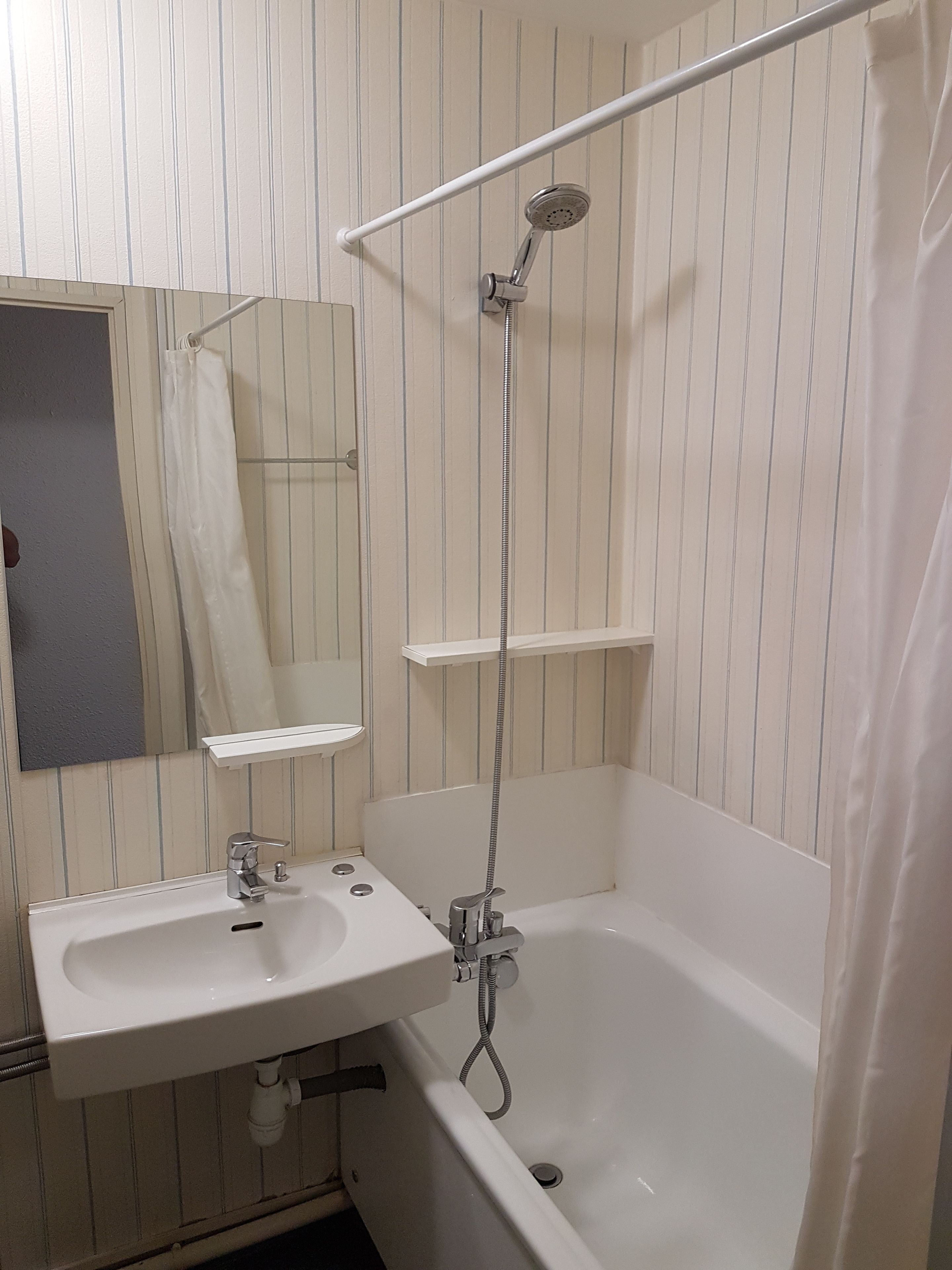 Een badkamer met een witte badkuip, een wastafel en een douche met een handdouche.