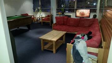 A living room with a pool table, a red sofa, a wooden coffee table, and a television on a stand.