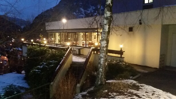 A building with a covered outdoor seating area, snow on the ground, and a mountain in the background. - Hôtel Inn Design Moutiers (Moutiers)