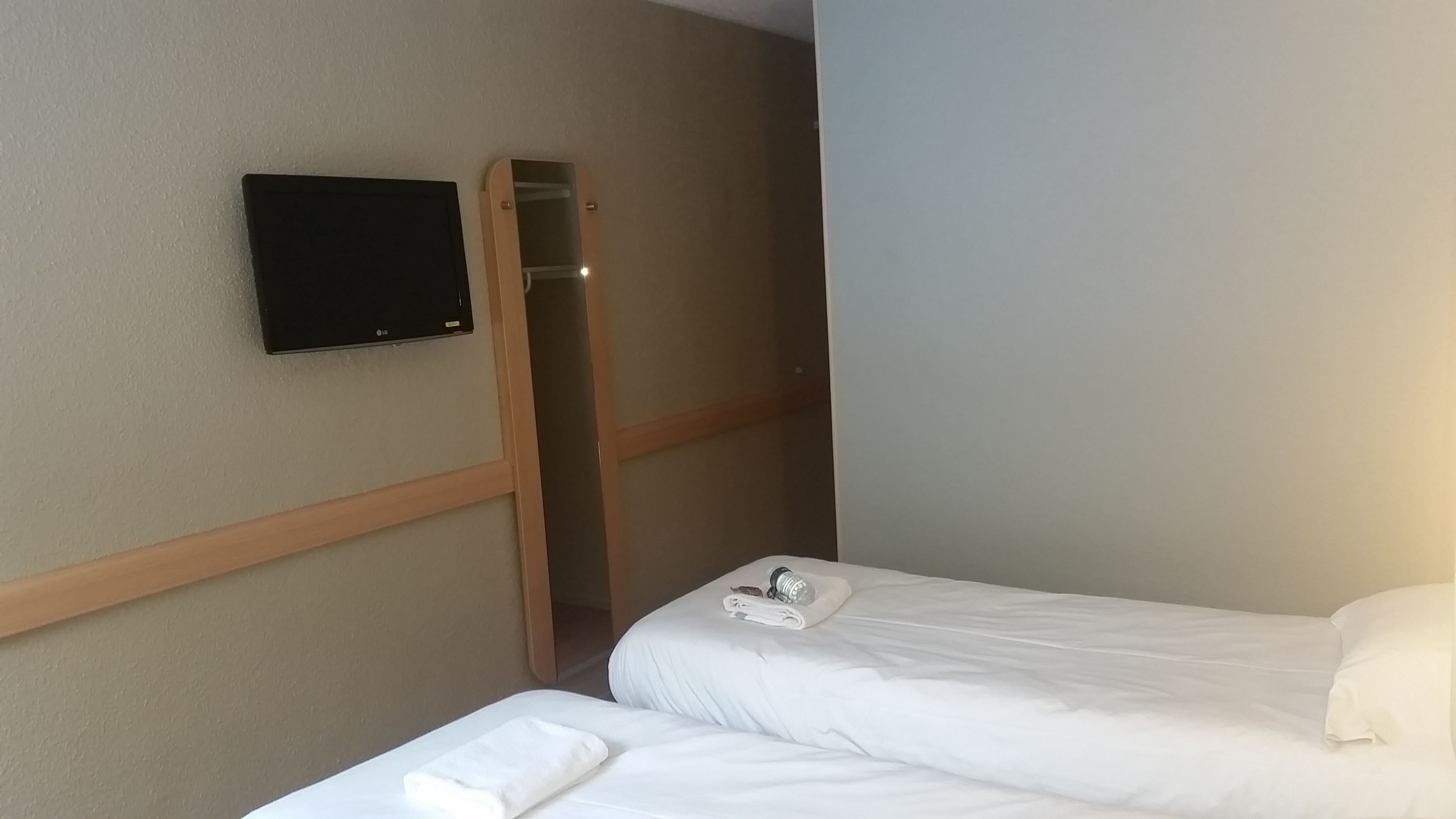 Habitación de hotel con cama, televisor montado en la pared y detalles en paneles de madera.