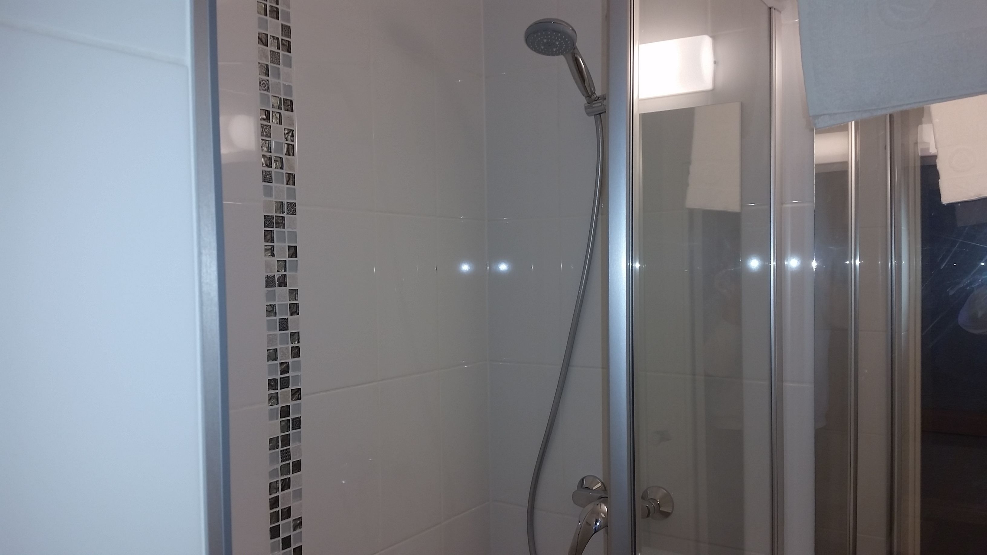 Een douchecabine met glazen wanden, een handdouche en een wandmengkraan.