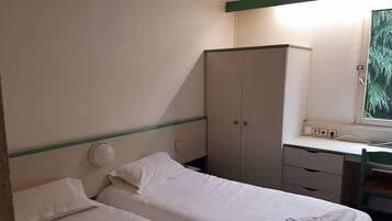 Ett hotellrum med två sängar, en garderob, ett skrivbord med en spegel och ett fönster med utsikt över träd.