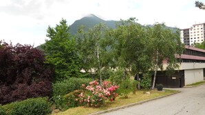 A residential street with a mountain in the background, a building with a gated entrance, and a variety of greenery including bushes and trees. - Hôtel Inn Design Moutiers (Moutiers)