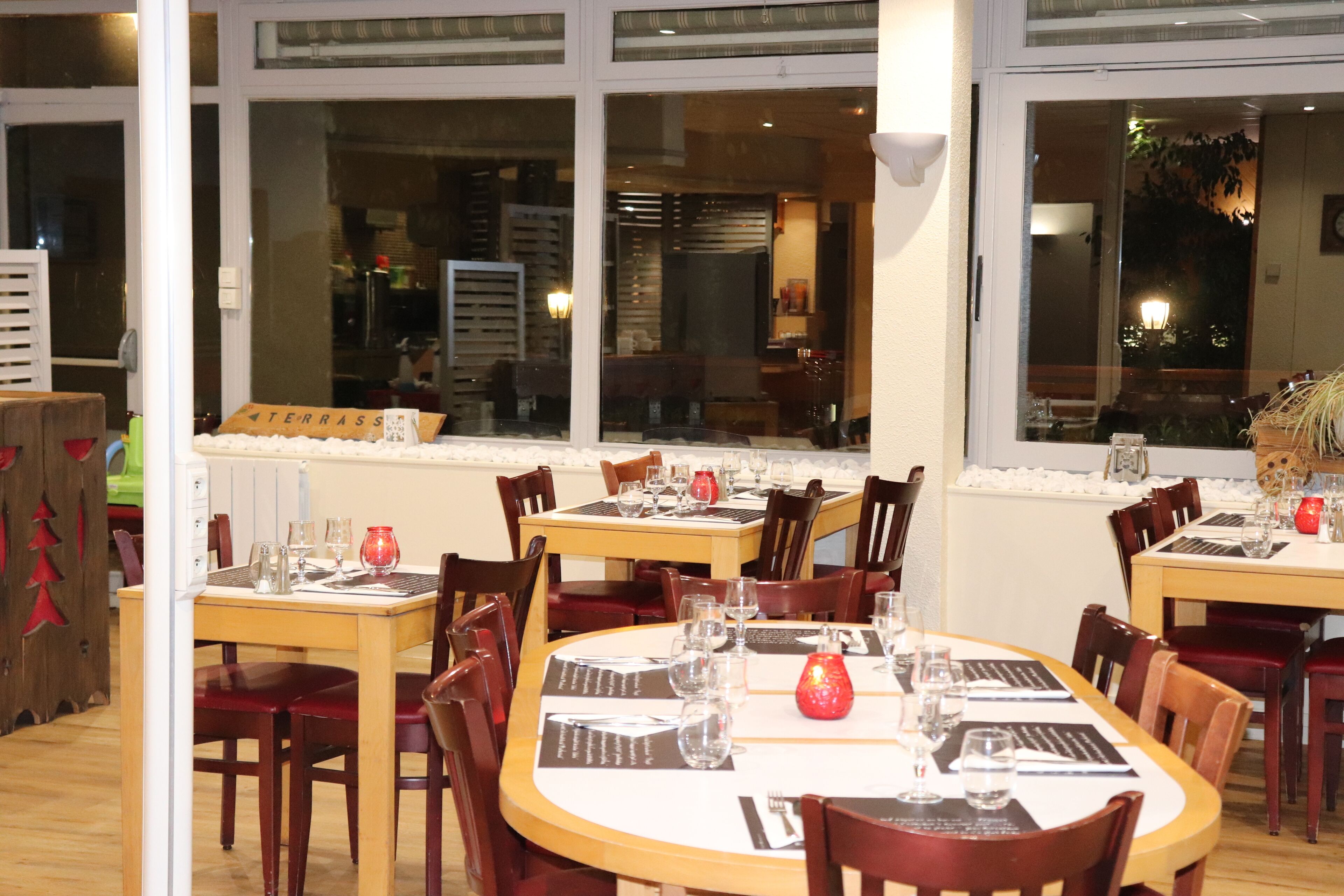 Un restaurant avec de nombreuses tables dressées pour le service, chacune étant équipée de menus, de verres et de couverts.