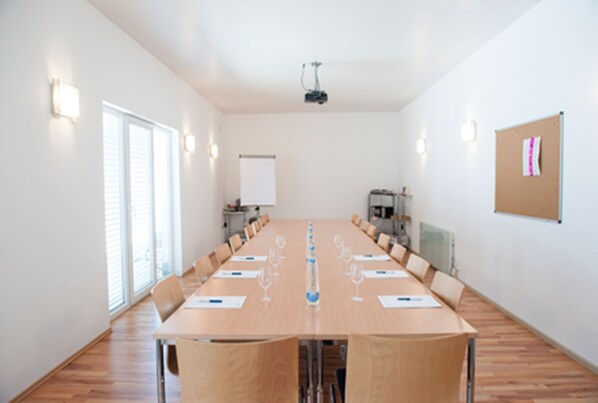 Un salón de conferencias con una larga mesa, sillas, un proyector y una pizarra.