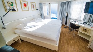 A hotel room with a bed, bedside table, desk, chair, and artwork on the wall. - Hotel Restaurant Hohberg (Schaffhausen)