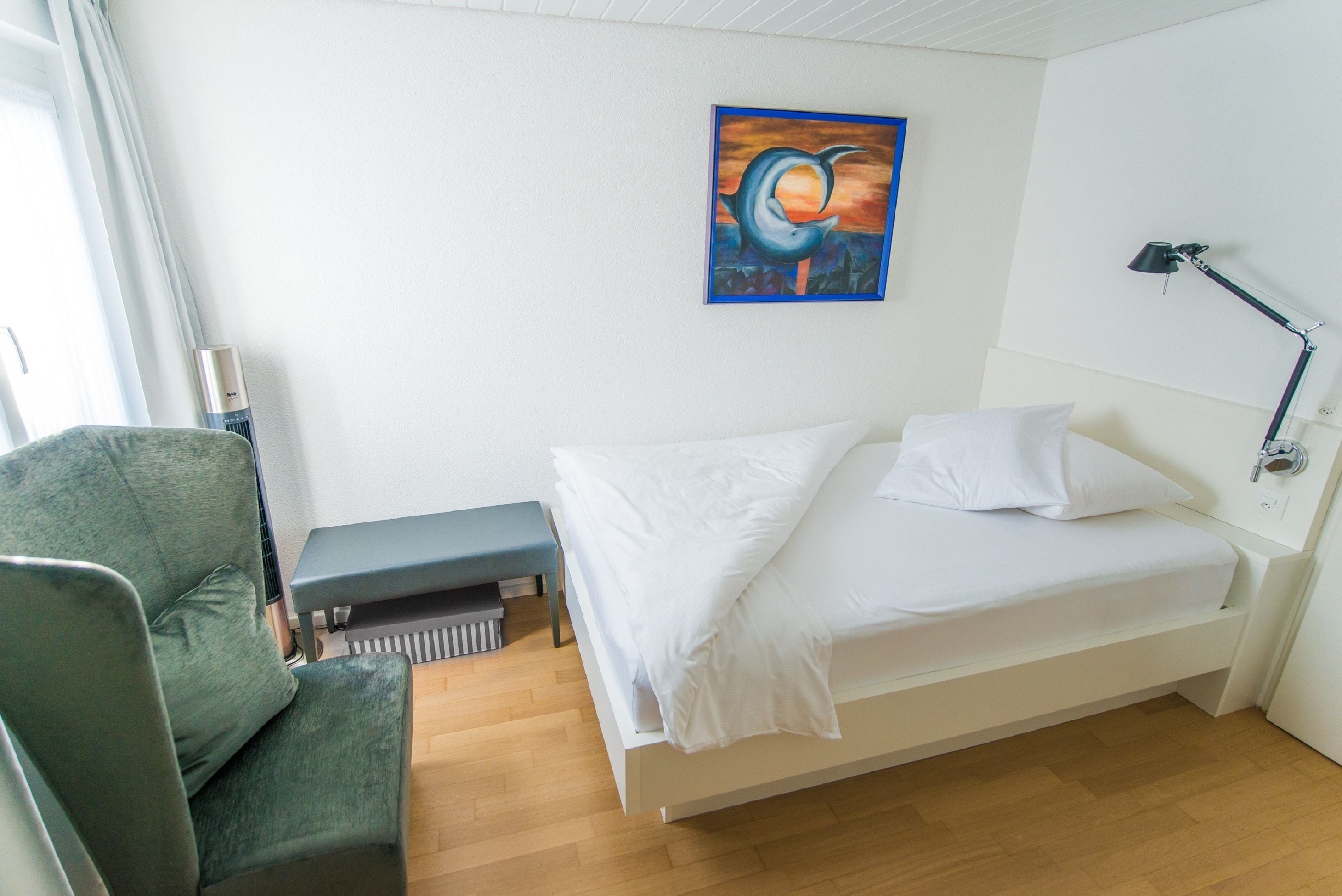 A hotel room with a bed, a bench, a desk, and a painting on the wall.