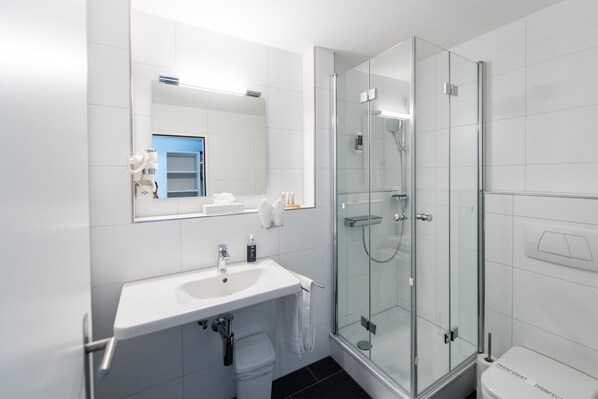 Un baño moderno con ducha envuelta en vidrio, un lavamanos blanco y un espejo sobre él.