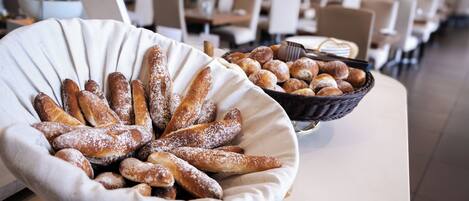 A buffet table with a variety of pastries and bread, including a large white bowl filled with breadsticks and a wicker basket with assorted pastries.