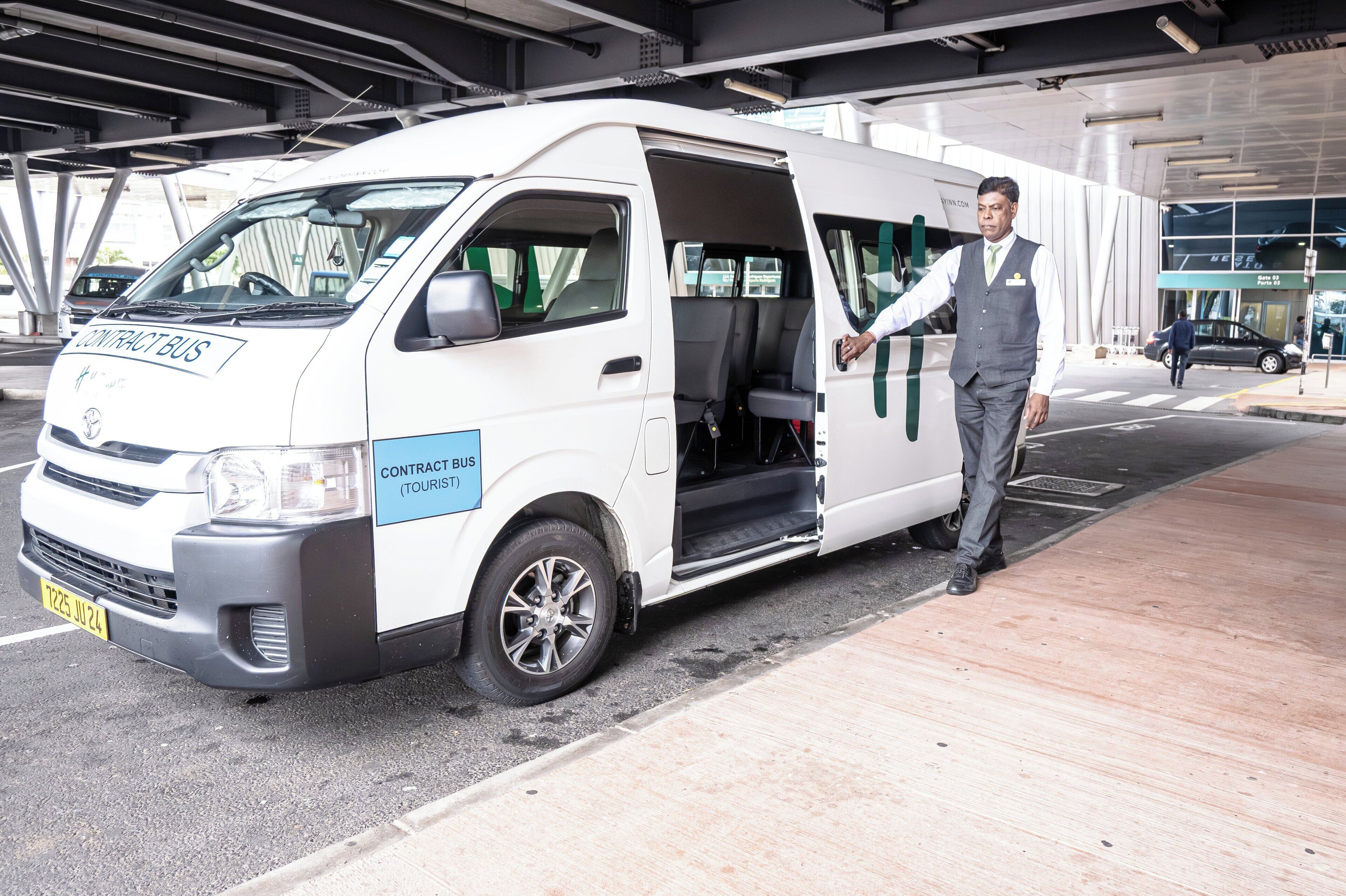 A white van with 'CONTRACT BUS TOURIST' written on the side parked at a bus station.