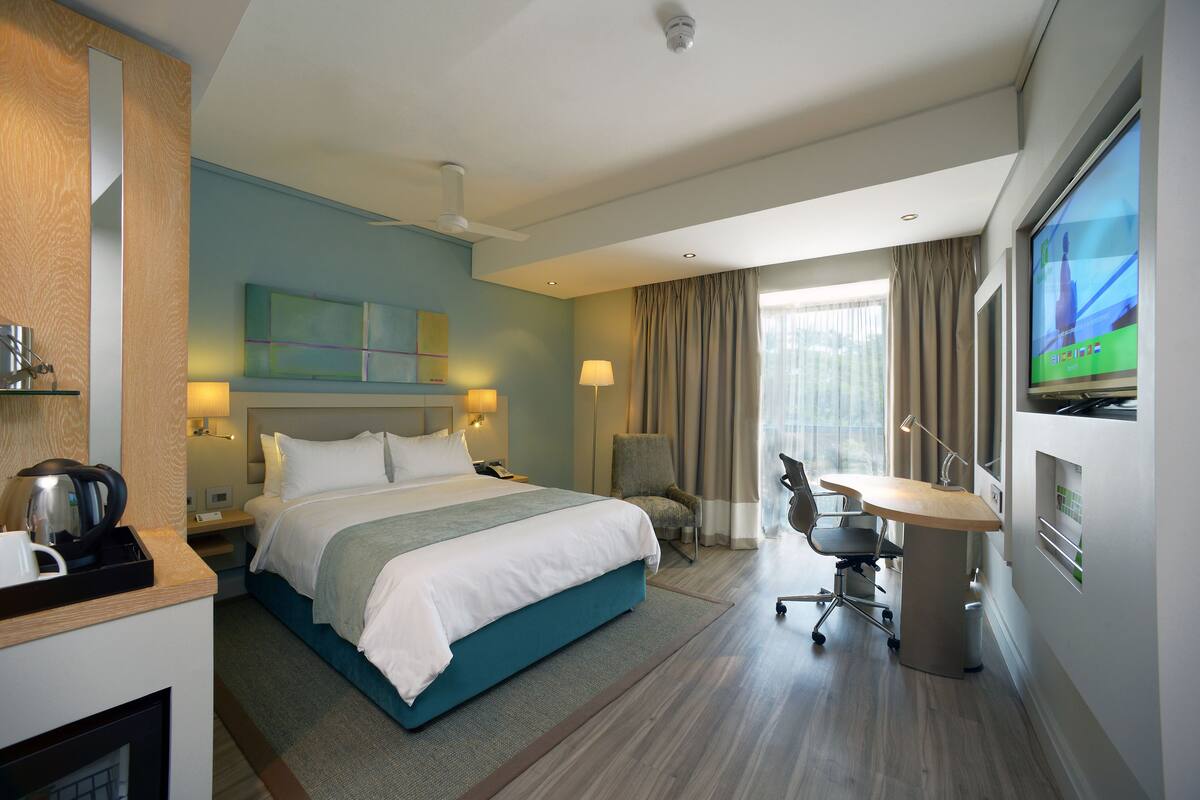 Une chambre d’hôtel moderne, dotée d’un grand lit, d’un bureau avec une chaise, d’une télévision et d’une fenêtre avec des rideaux.