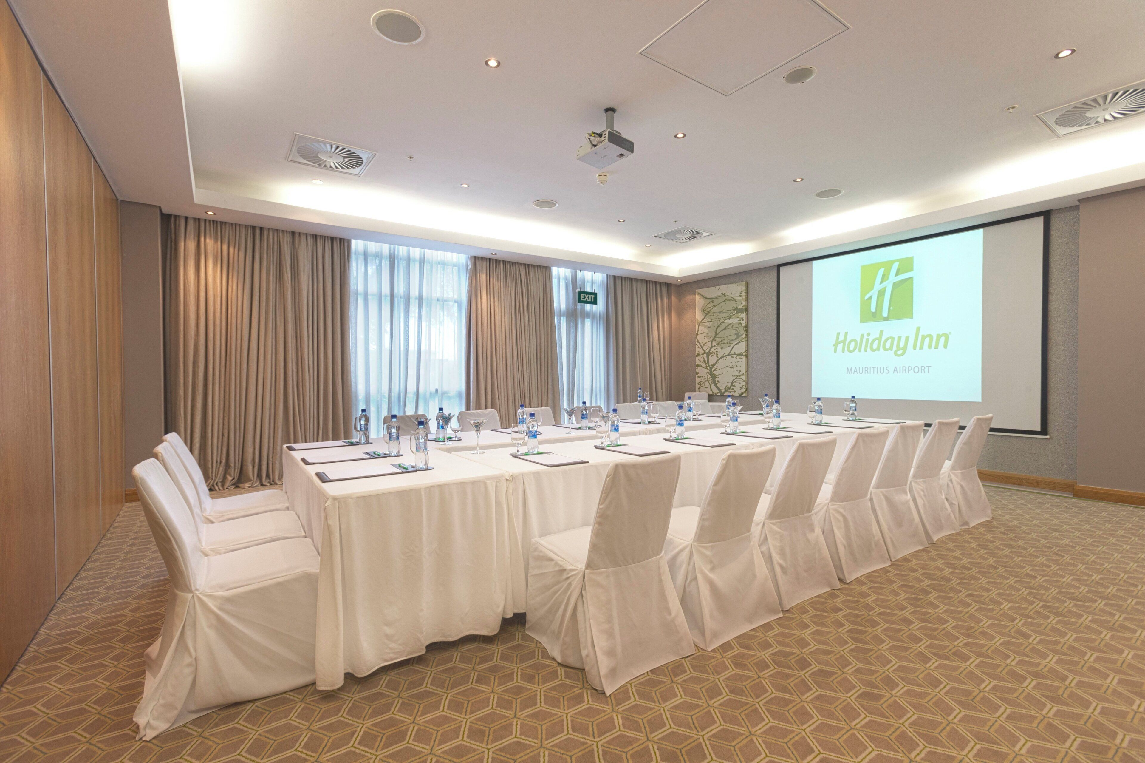 A conference room with a long table, chairs, and a projector screen displaying the Holiday Inn logo.