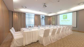 A conference room with a long table, chairs, and a projector screen displaying the Holiday Inn logo.