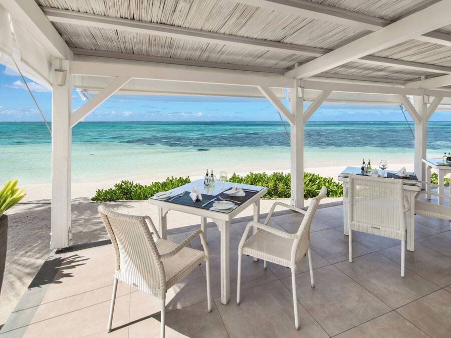 Een overdekte buitenruimte met tafels en stoelen, met uitzicht op een strand en de oceaan.