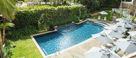 A swimming pool surrounded by lush greenery, with lounge chairs and umbrellas.