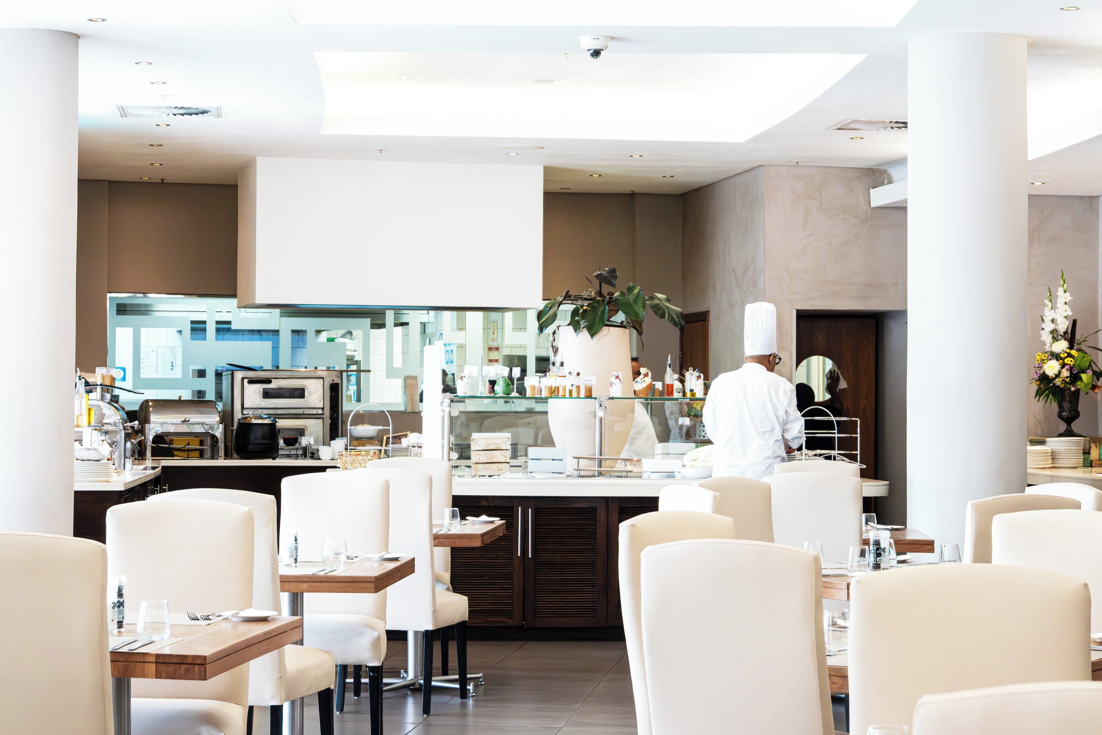 A modern restaurant with a central bar area, seating for guests, and a visible kitchen.
