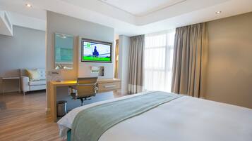 A modern hotel room with a large bed, a desk with a chair, a television, and a window with curtains.