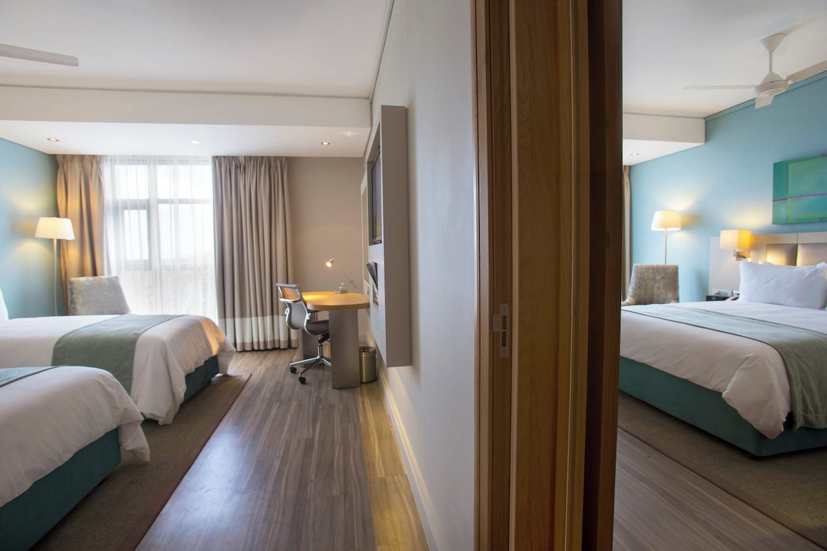 Quarto de hotel com duas camas, uma escrivaninha e uma cadeira.