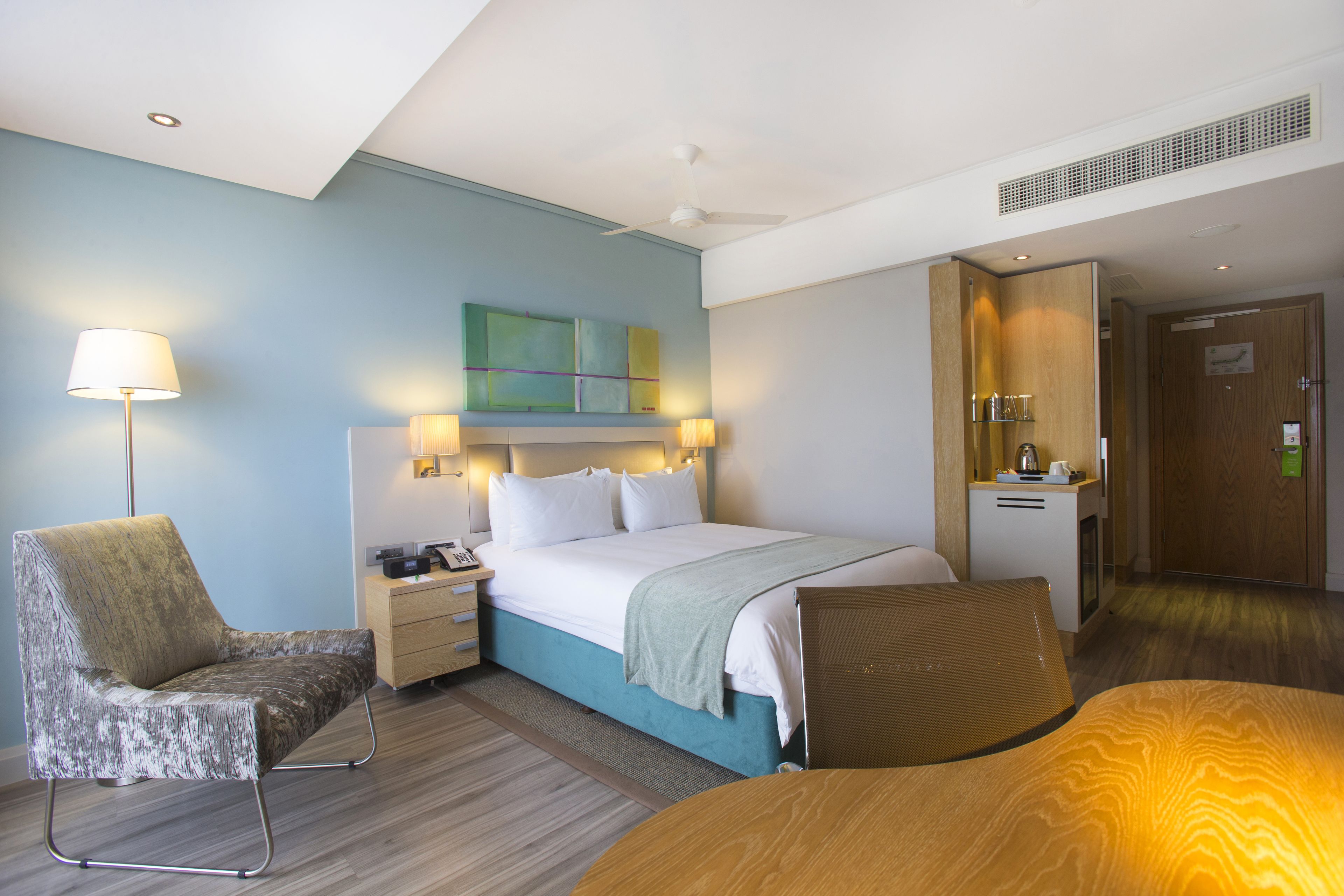 A hotel room with a bed, a chair, a desk, and a lamp.