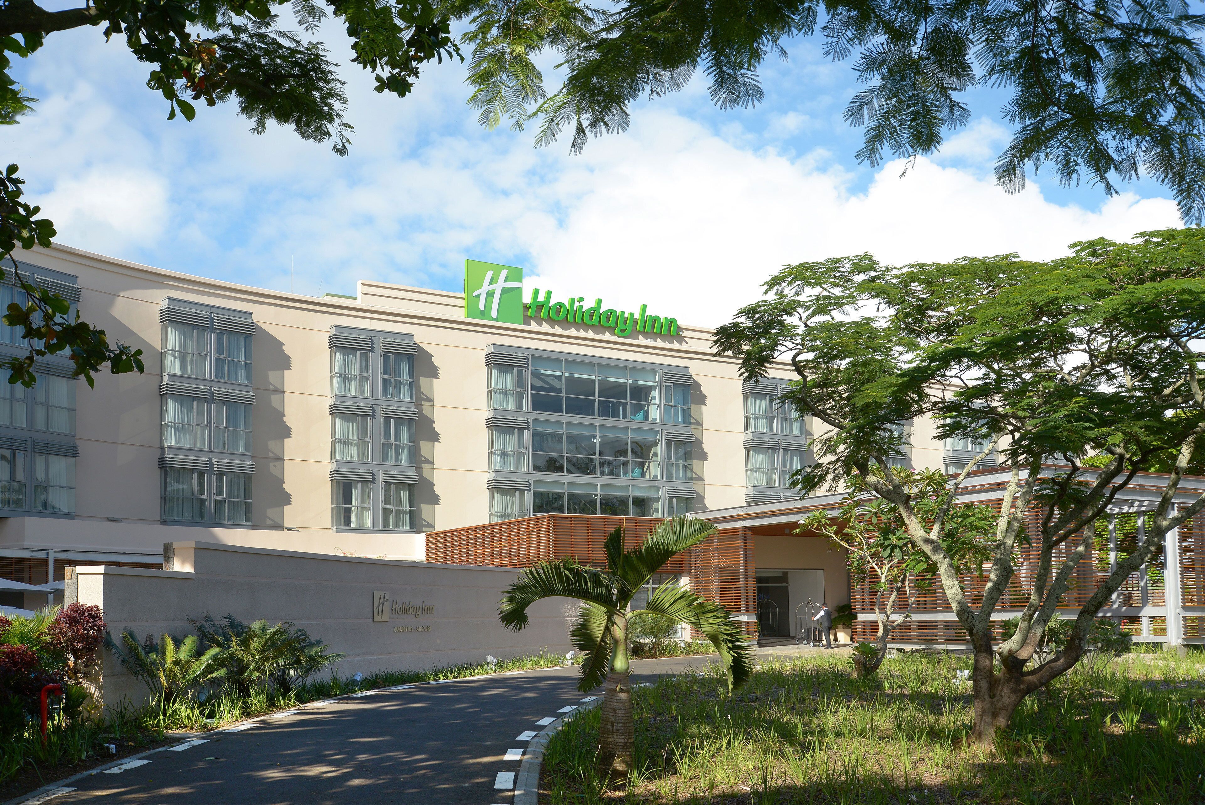 A Holiday Inn hotel with a modern facade, large windows, and a well-maintained garden area.