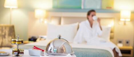 A hotel room with a neatly arranged breakfast table, a bed with a white comforter, and a painting on the wall.