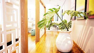 Un couloir doté d’un plancher en bois, d’une cloison décorative blanche et d’un grand vase blanc contenant une plante.