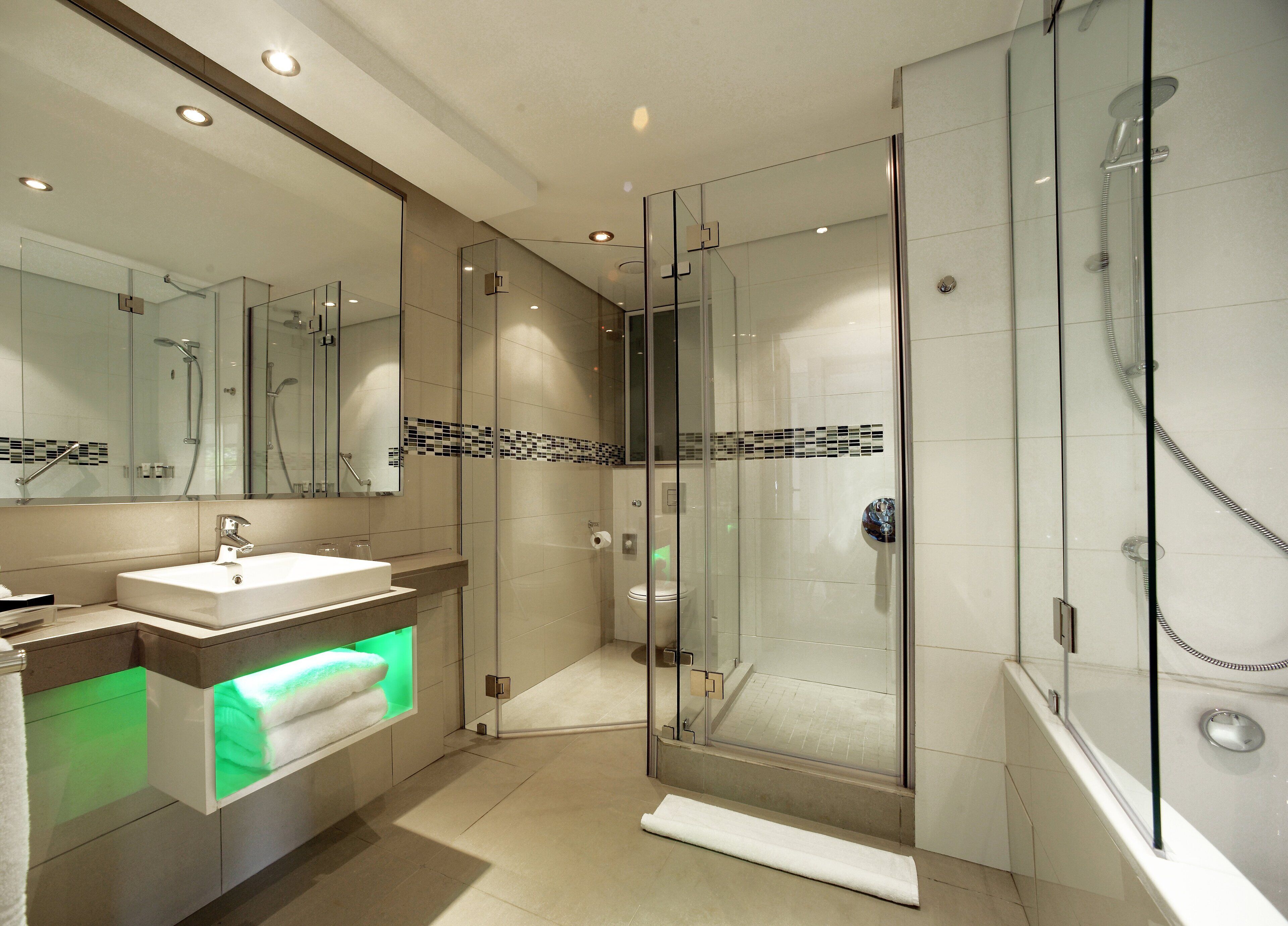 Un baño moderno con ducha envuelta en vidrio, lavamanos con espejo y un perchero para toallas.