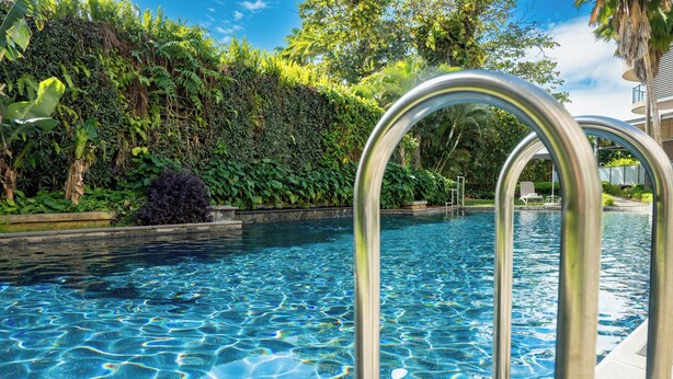 A swimming pool with clear water, surrounded by lush greenery and a metal pool ladder. - Holiday Inn Mauritius Mon Tresor by IHG (Plaine Magnien)