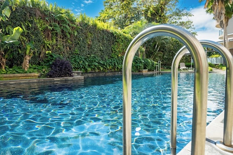 A swimming pool with clear water, surrounded by lush greenery and a metal pool ladder.