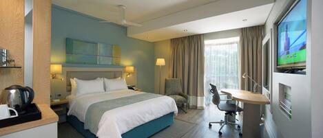 A hotel room with a bed, desk, chair, television, and a view of the outdoors.