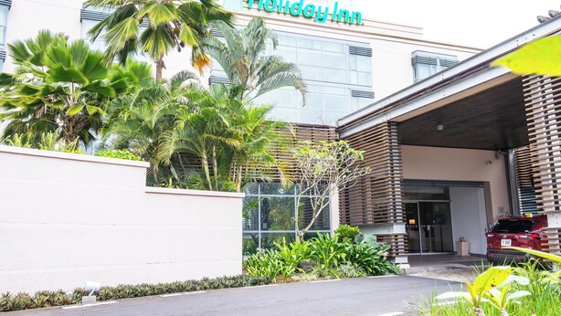 A Holiday Inn hotel with a modern facade, palm trees, and a red car parked outside. - Holiday Inn Mauritius Mon Tresor by IHG (Plaine Magnien)