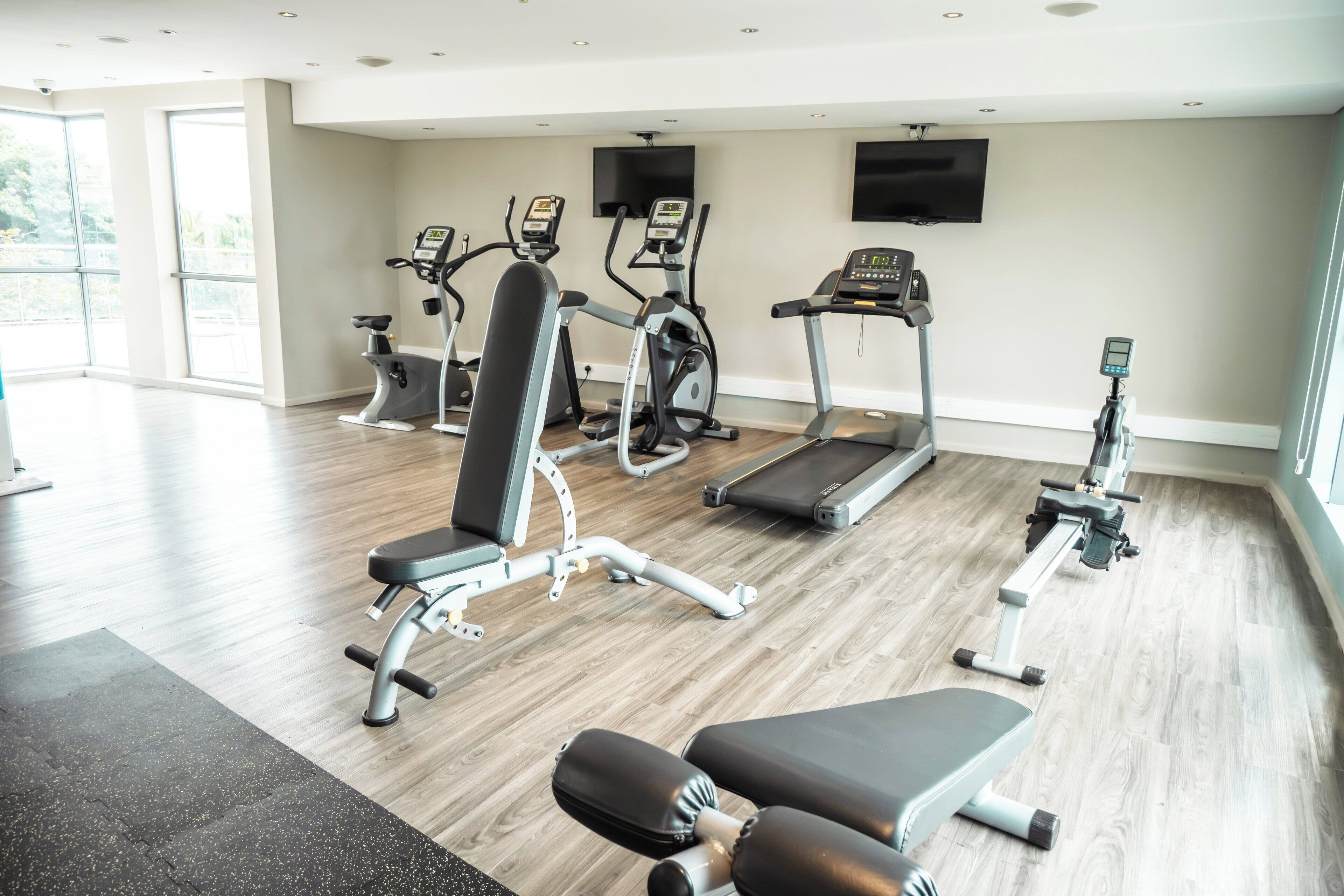 A gym with various exercise equipment, large windows, and a flat-screen TV on the wall.