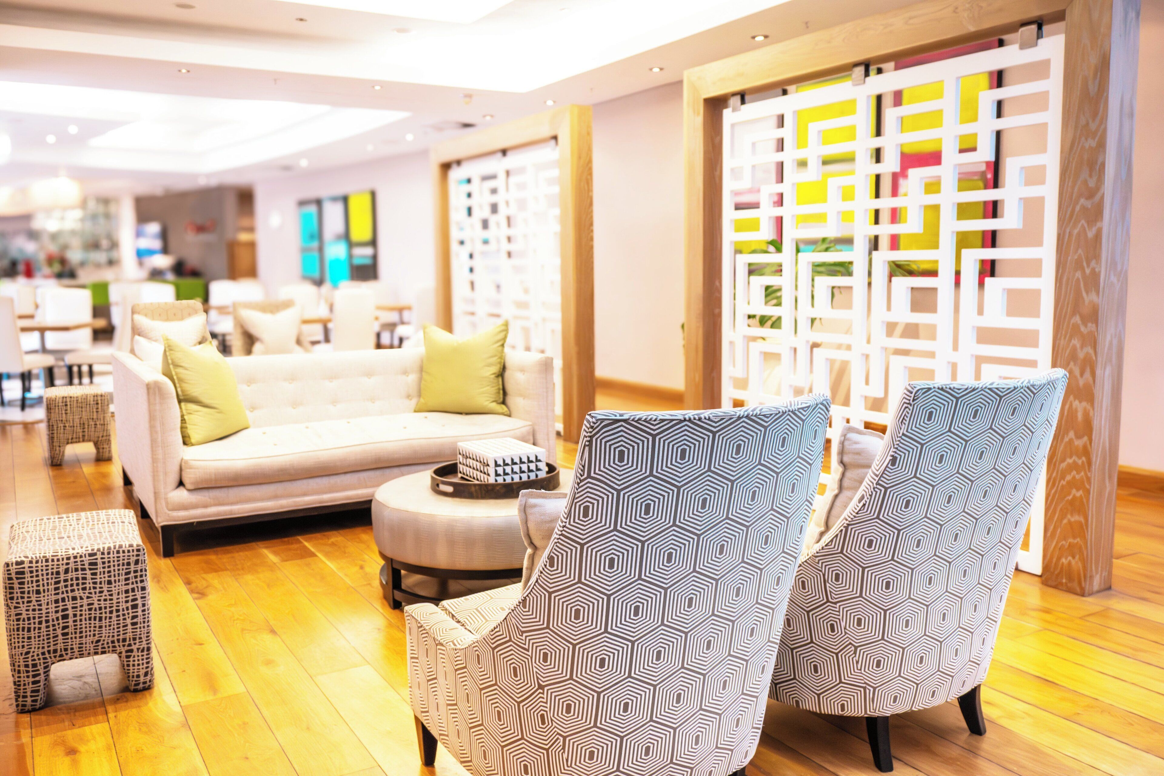 Un moderno vestíbulo de hotel con un sofá, sillones y un separador decorativo.