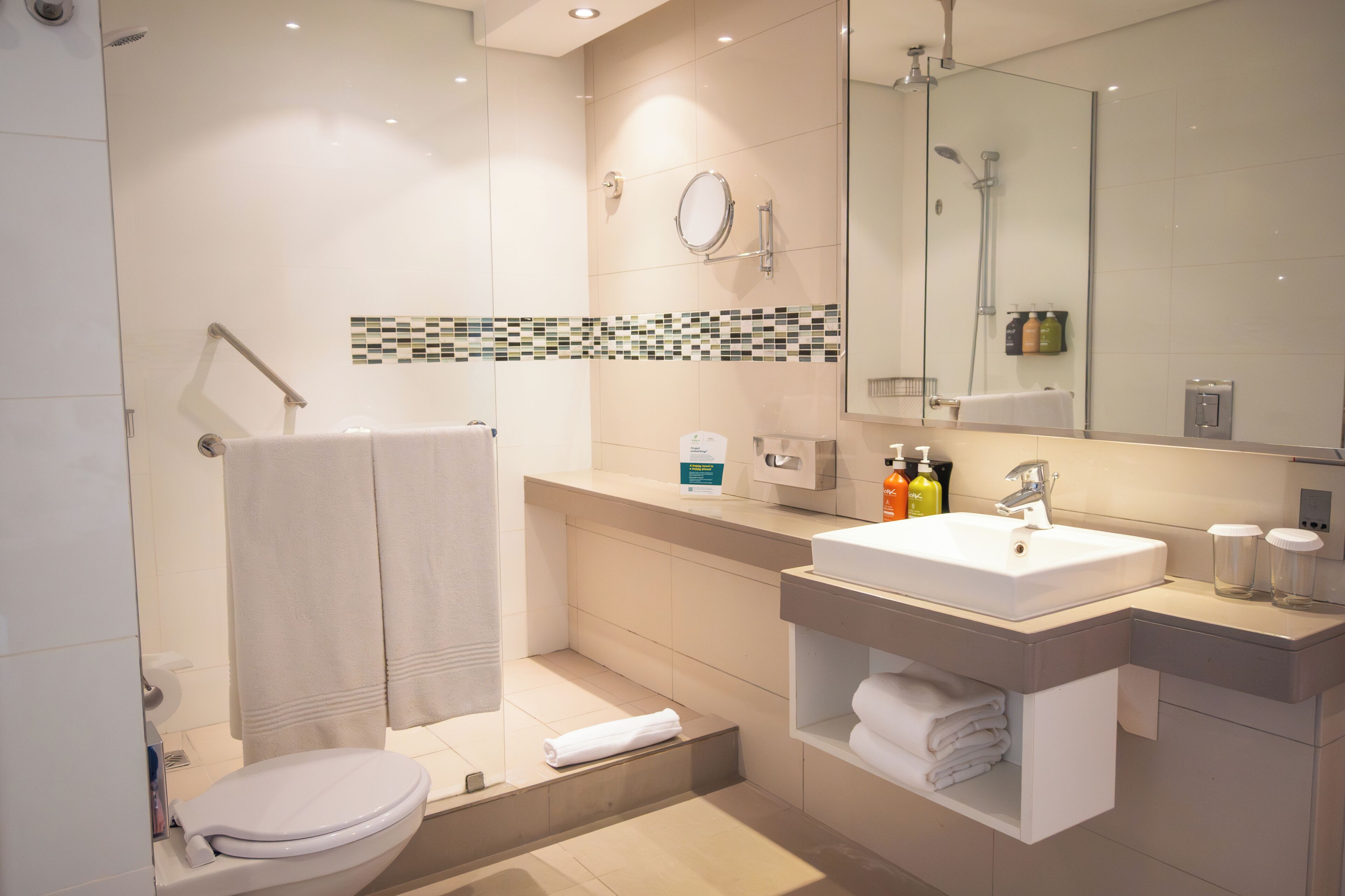 A modern bathroom with a shower, toilet, sink, and a mirror.