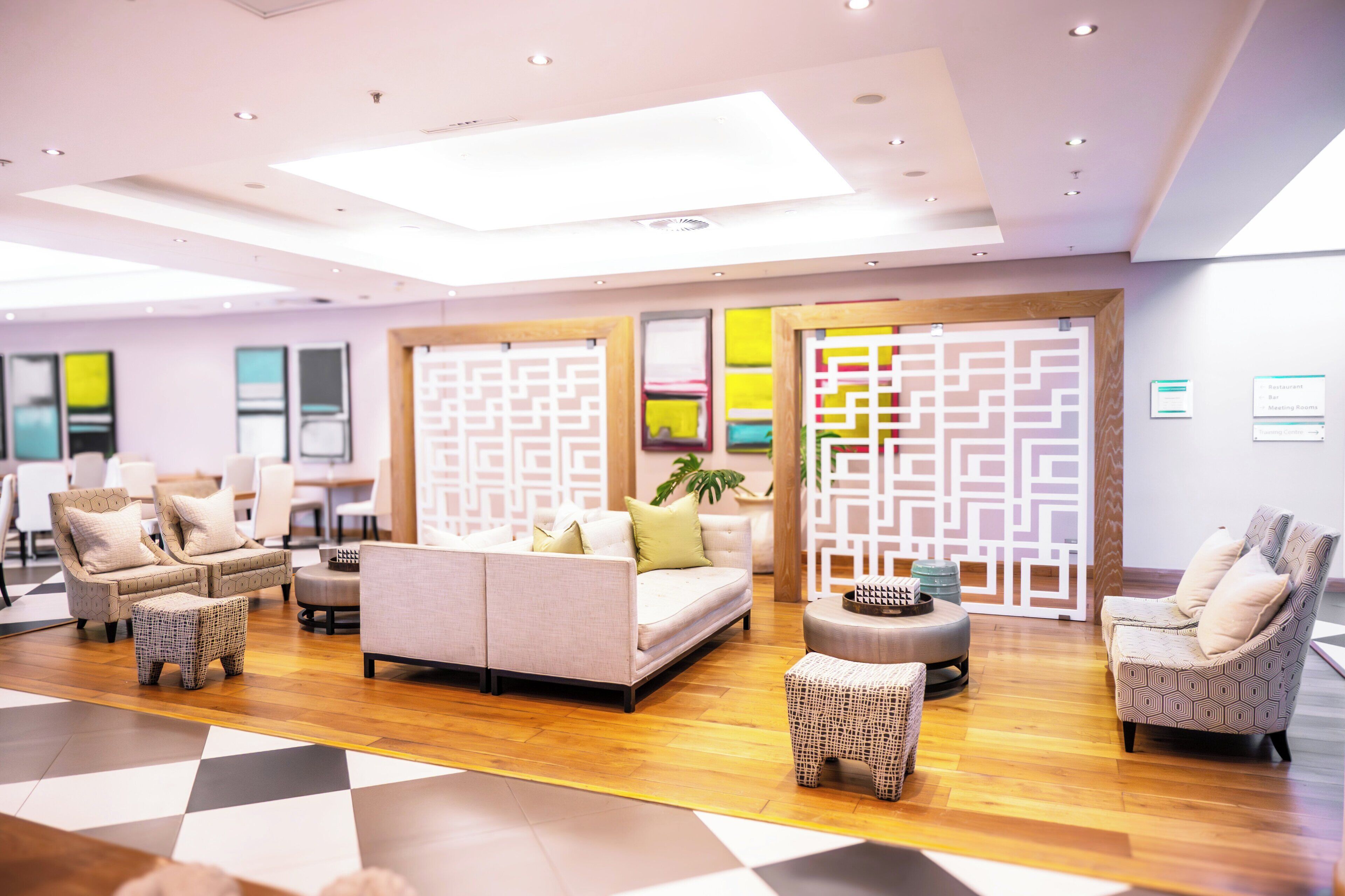 A modern lounge area with sofas, chairs, and a coffee table, featuring a geometric patterned partition and a wooden floor.