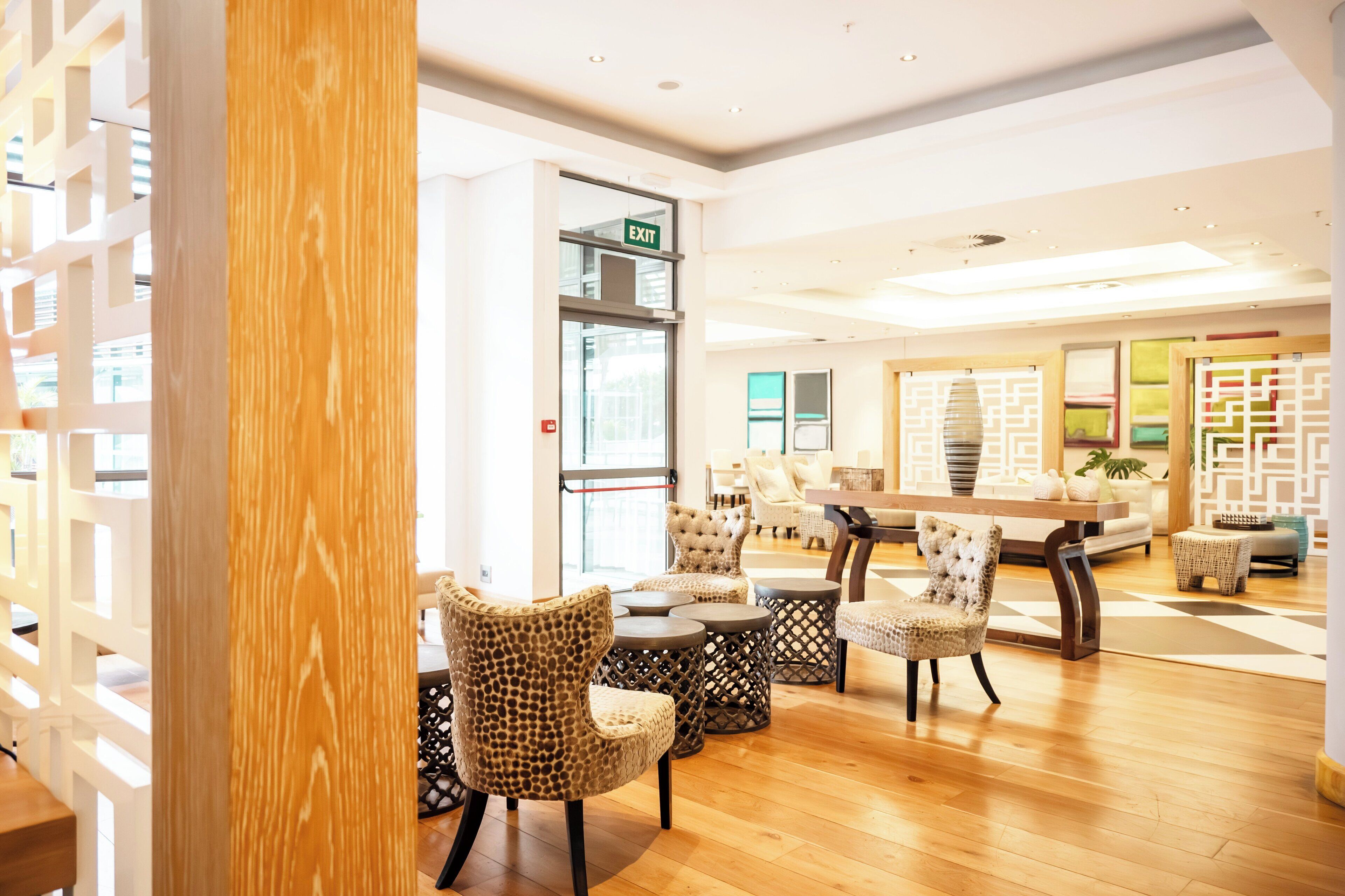 A spacious lobby with a wooden floor, a reception desk, and a seating area with patterned chairs and a sofa.