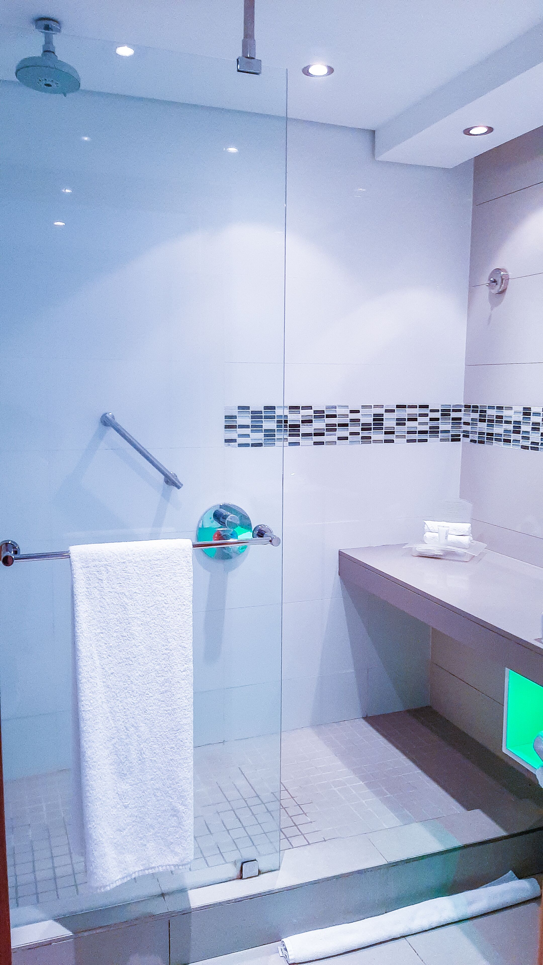 A modern bathroom with a glass shower enclosure, a white towel hanging on a rack, and a tiled backsplash.