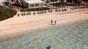 An aerial view of a beach with sun loungers, a few people, and a boat near the shore. - Holiday Inn Mauritius Mon Tresor by IHG (Plaine Magnien)