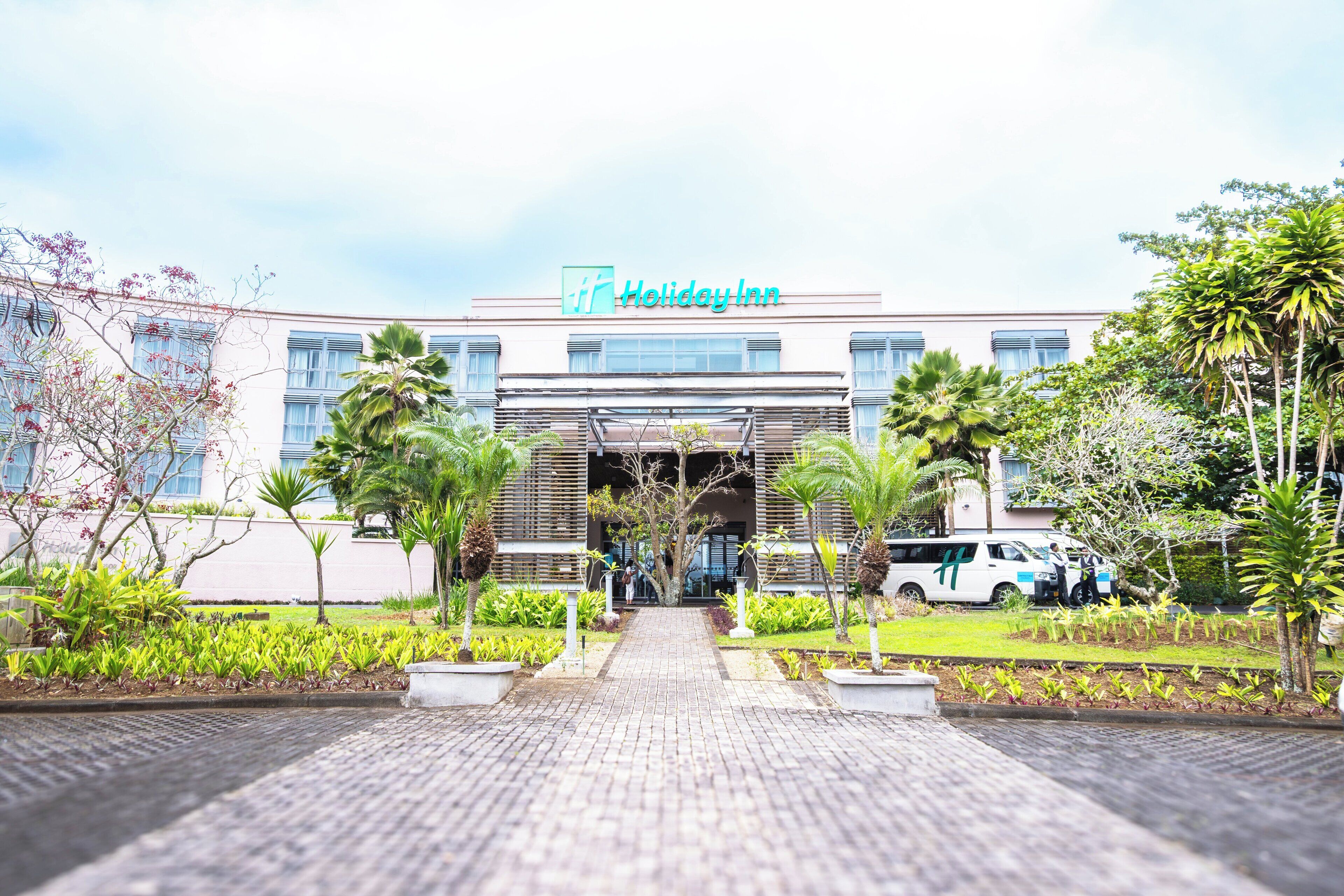 Un hotel Holiday Inn con fachada moderna, entrada principal y un jardín bien cuidado.