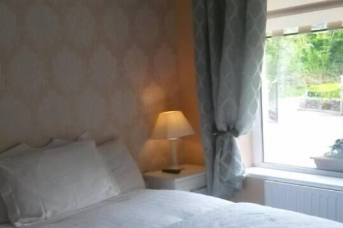 A neatly made bed with a patterned duvet, a bedside lamp, and a window with curtains.