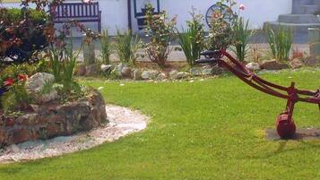 Un jardín con una herramienta roja de jardinería, un muro de piedra y diversas plantas.