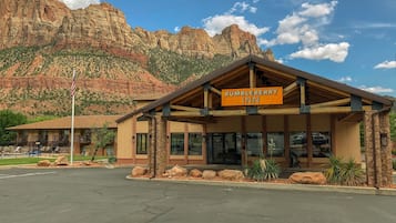 A BUMBLEBERRY INN with a mountain backdrop, featuring a stone facade, large windows, and a wooden roof structure.