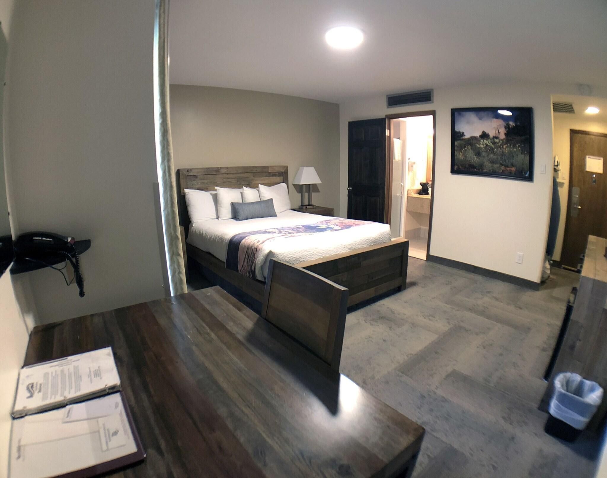 A bedroom with a bed, bedside table, lamp, and a painting on the wall.