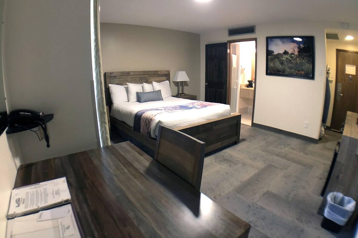 A bedroom with a bed, bedside table, lamp, and a painting on the wall.