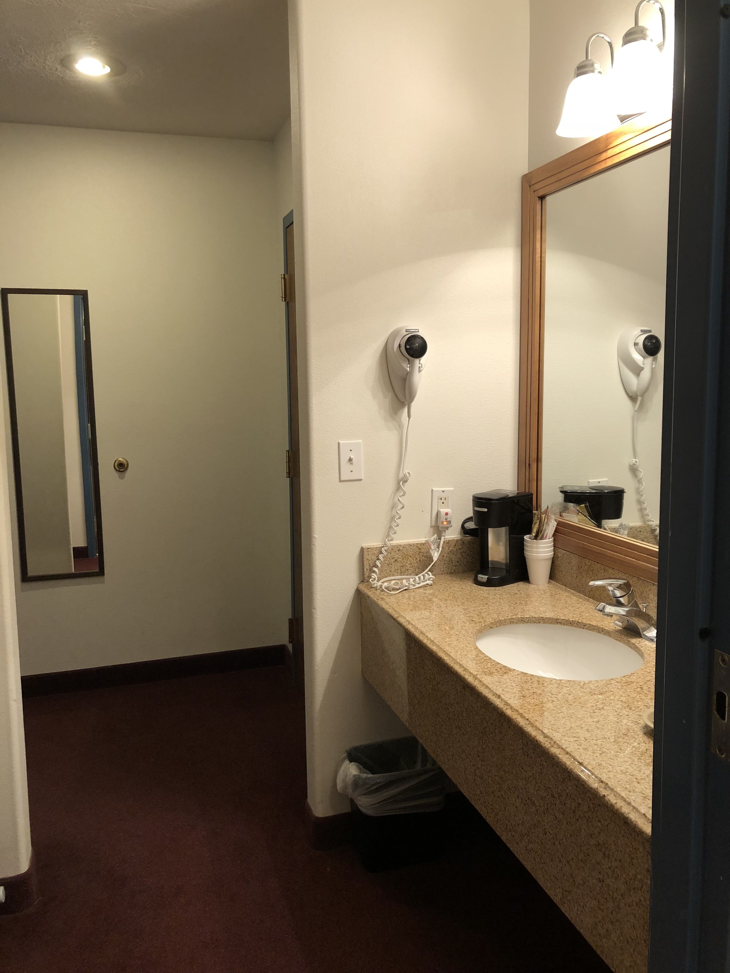Een hotelbadkamer met een wastafel, spiegel, haardroger en een prullenbak.