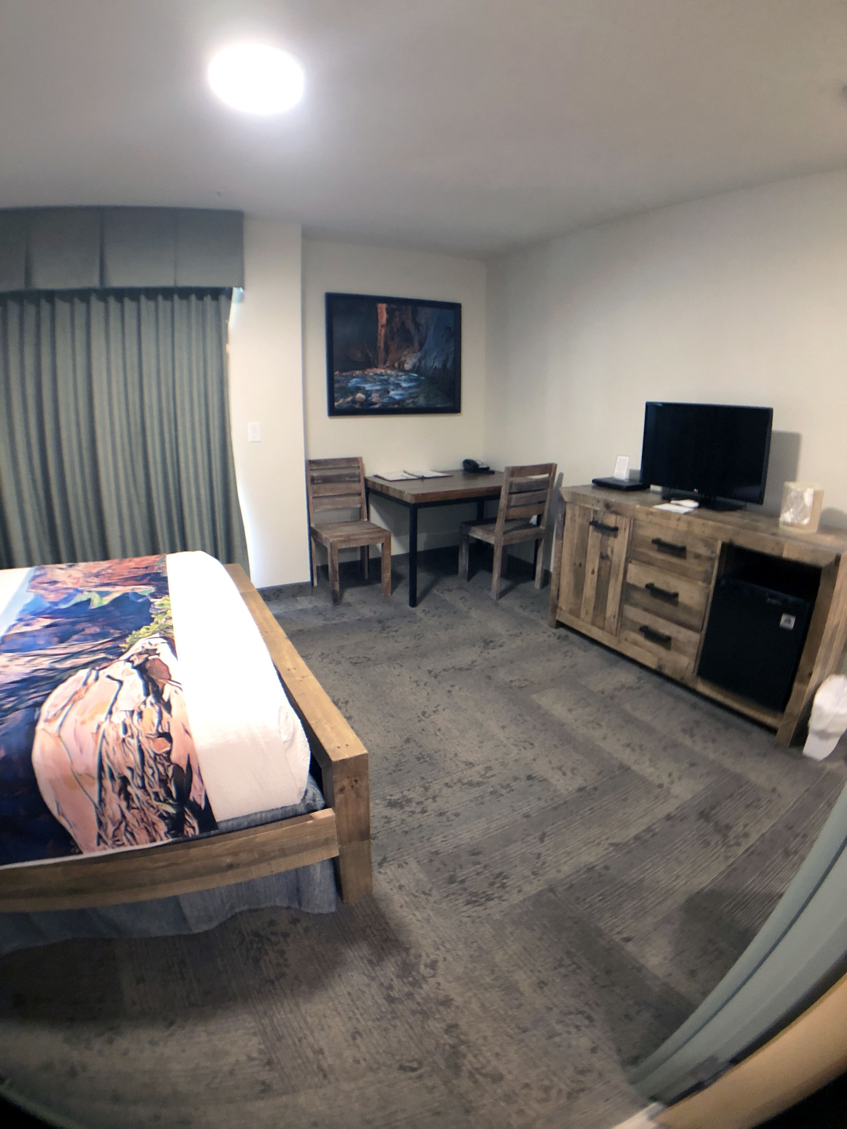 Ett hotellrum med en säng, ett skrivbord, en tv och en tavla på väggen.