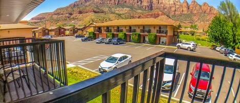A hotel with a parking lot, a mountain view, and a balcony with a railing.