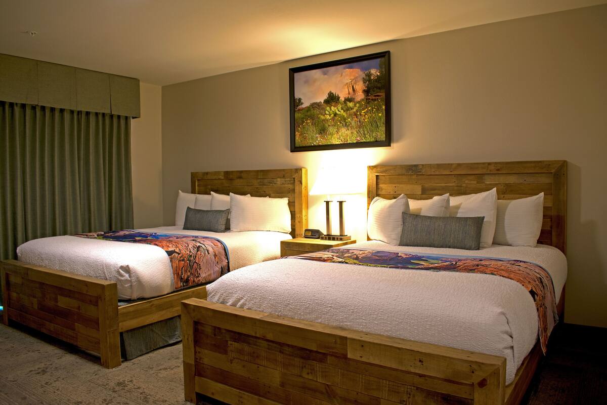 A hotel room with two wooden beds, a nightstand with a lamp, and a painting on the wall.