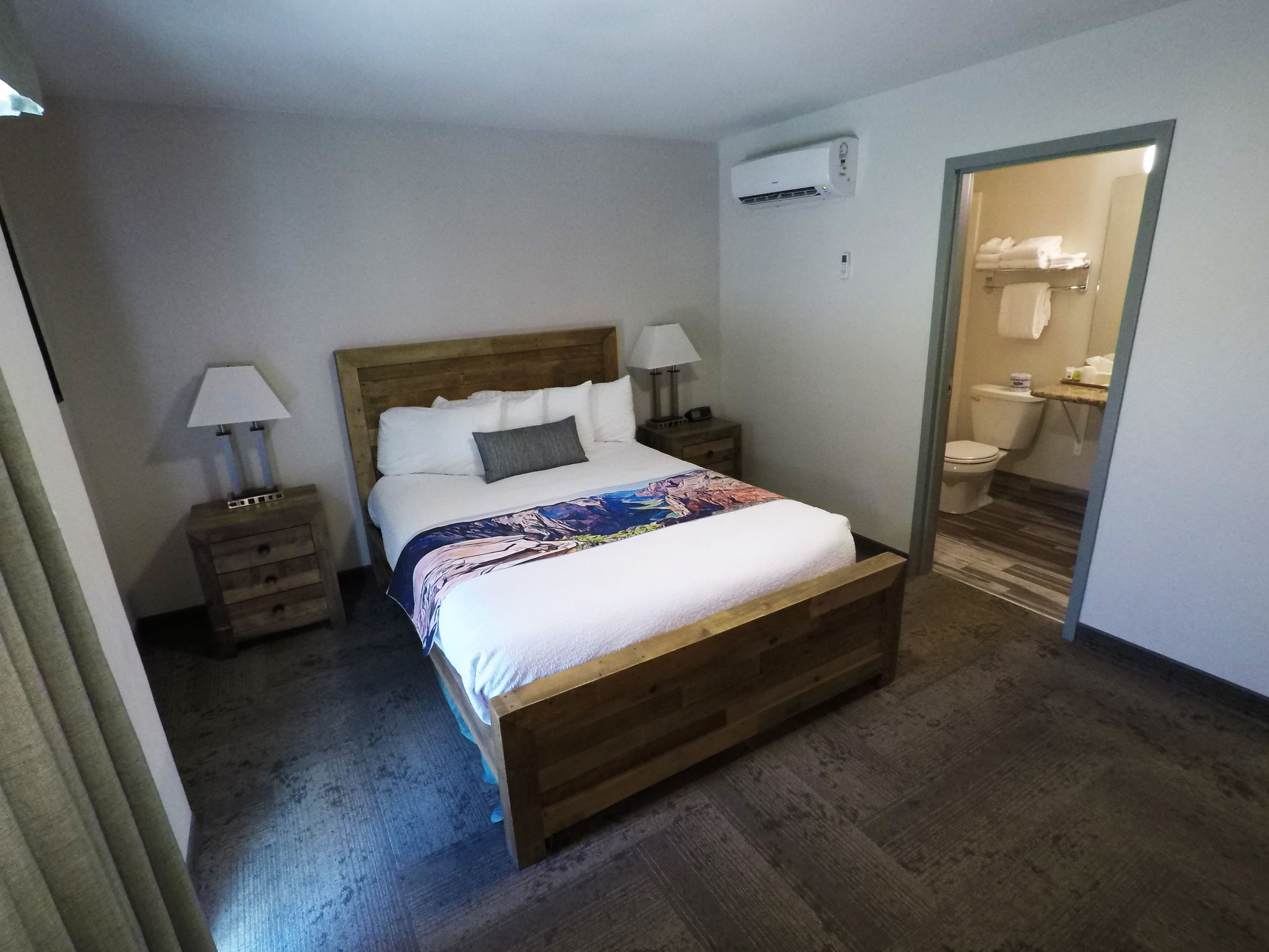 Une chambre à coucher avec un lit en bois, du linge de lit blanc, une table de chevet avec une lampe et un climatiseur fixé au mur.